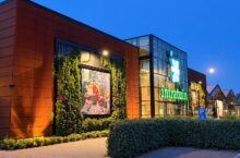De verlichte ingang van tuincentrum Intratuin Lisse in de avondschemering, met groene gevelbeplanting