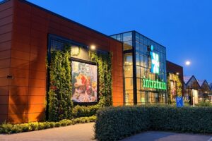 De verlichte ingang van tuincentrum Intratuin Lisse in de avondschemering, met groene gevelbeplanting